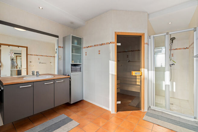 Deze ruime villa met maar liefst 5 slaapkamers en 3 badkamers is gelegen in een residenti&euml;le woonwijk, op een perceel van 15a85ca.

Bij het betreden van de woning komt men in de inkomhal met apart gastentoilet. In 2002 werd de woning uitgebreid met een a