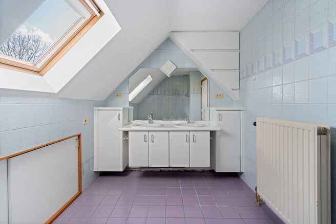 Deze ruime villa met maar liefst 5 slaapkamers en 3 badkamers is gelegen in een residenti&euml;le woonwijk, op een perceel van 15a85ca.

Bij het betreden van de woning komt men in de inkomhal met apart gastentoilet. In 2002 werd de woning uitgebreid met een a
